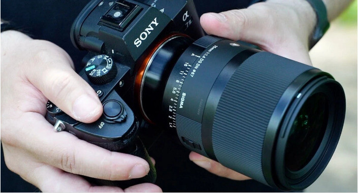 Камера Sony з об'єктивом Sigma 35mm f/1.4 DG DN Art у руках фотографа на вулиці з чітко видимою розміткою кільця діафрагми
