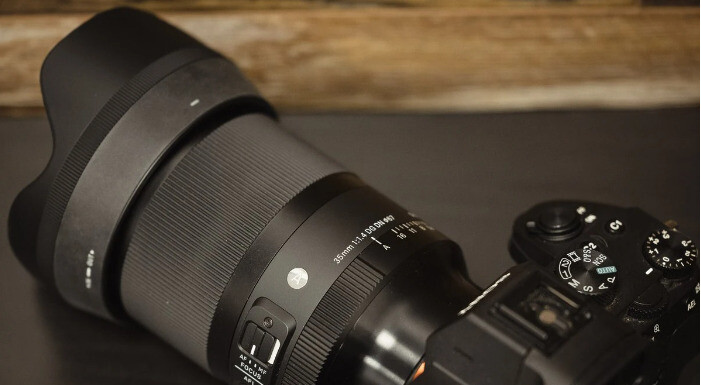 Об'єктив Sigma 35mm f/1.4 DG DN Art з блендою на камері Sony на темній стільниці з видимими перемикачами AF/MF та кнопкою AFL